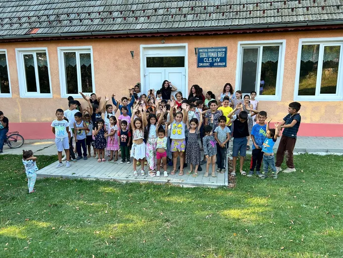 Grup de copii bucuroși în fața școlii primare
