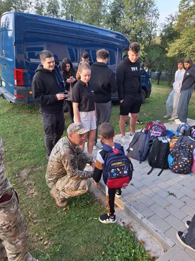 Voluntari predau ghiozdane noi unui copil, lângă duba cu donații